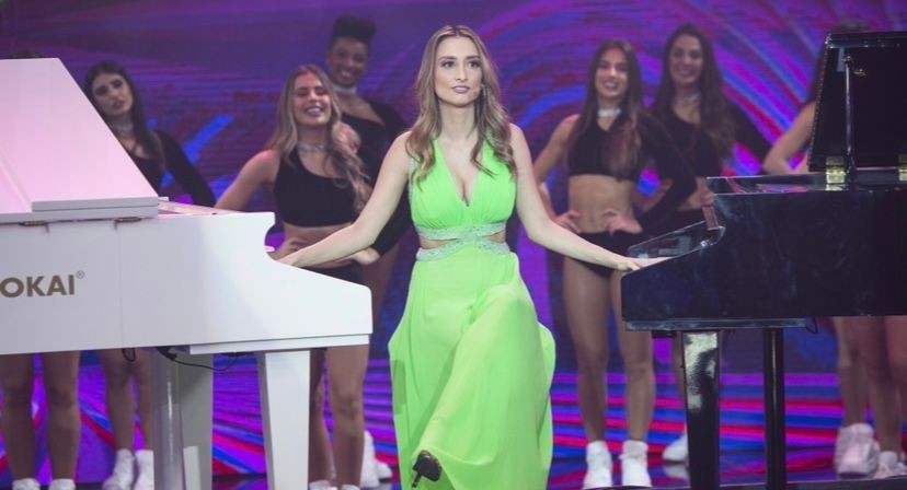 Woman in a neon dress performing between two pianos with dancers in the background.